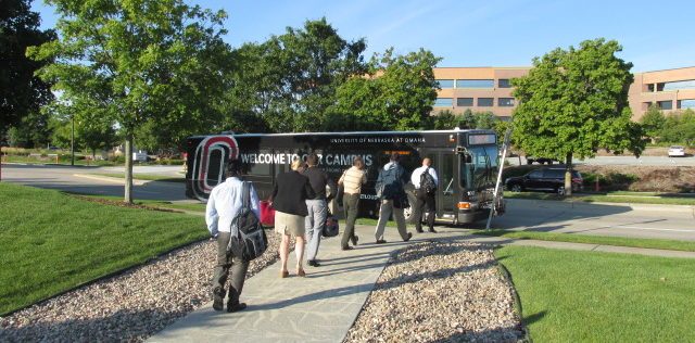 Riders walking toward wrapped Metro bus with UNO advertising