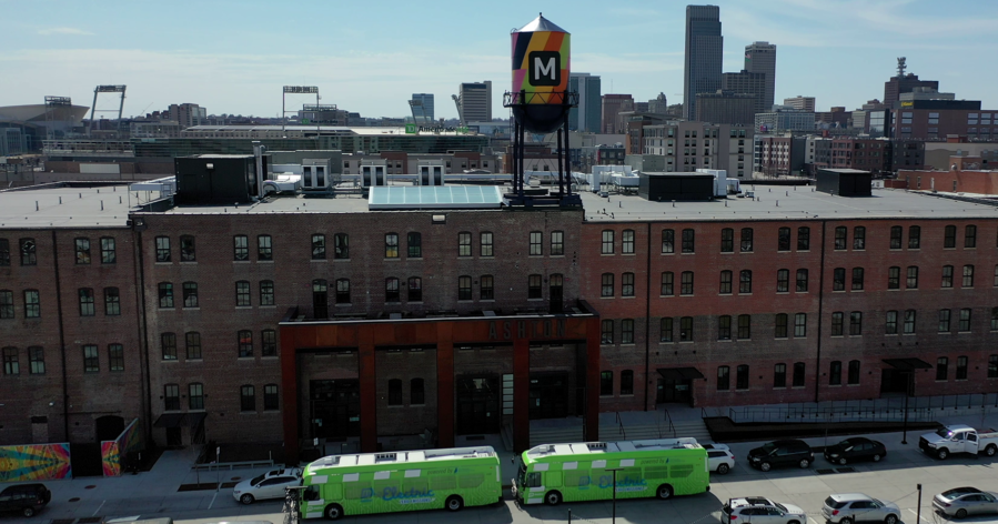 Photo of electric buses in front of Ashton Building, with Omaha skyline in the background