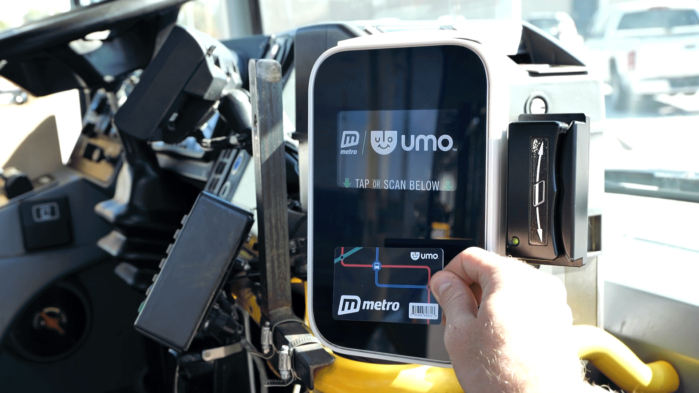 A bus rider pays their fare with a Umo smart card on the reader at the front of the bus